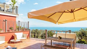 A terrace with a table, chairs, and an umbrella, overlooking a scenic view of the sea. - Terrazza Aphrodite - Two Bedroom Apartment, Sleeps 5 (Salerno)
