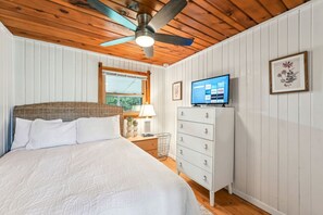 Une chambre à coucher avec un lit, une commode, un ventilateur de plafond, une télévision et une fenêtre.