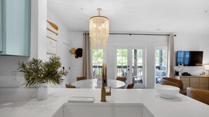A modern kitchen with a central island, a chandelier, and a dining area with chairs and a table.
