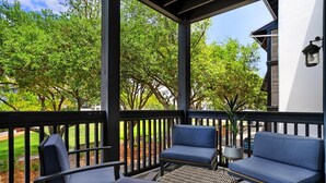 A covered outdoor seating area with two blue cushioned chairs and a small table, surrounded by a black railing.