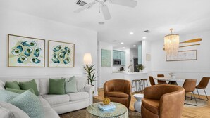 A modern living room with a white sofa, brown leather chairs, a glass coffee table, and artwork on the wall.