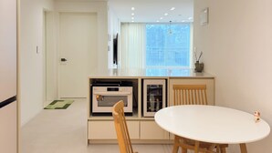 A modern kitchen with built-in appliances, a dining area with a white table and wooden chairs, and a view of the city through large windows.