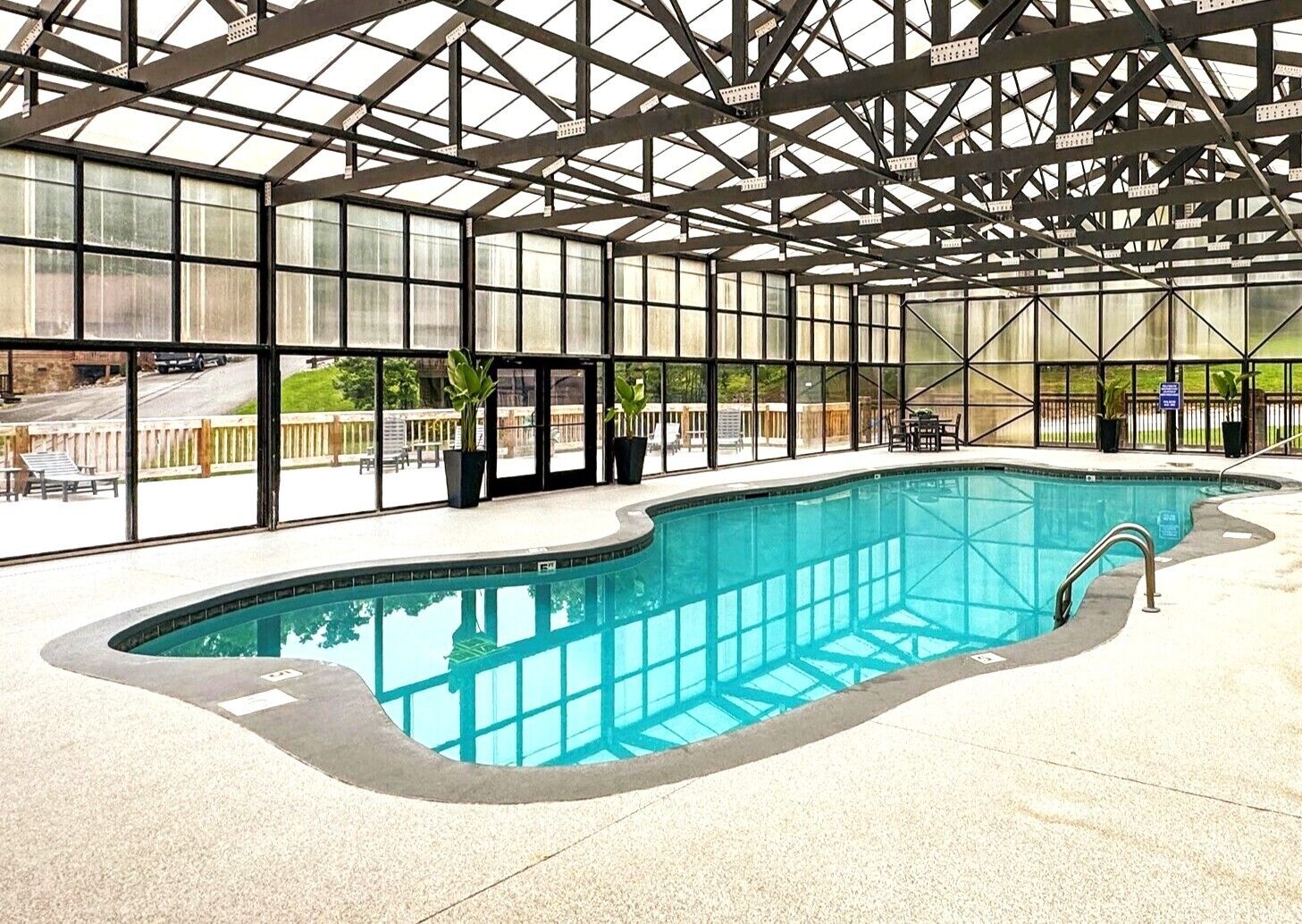 An indoor swimming pool with a glass ceiling, surrounded by a patio area with outdoor seating.