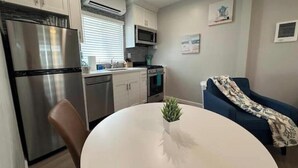 Une cuisine compacte équipée d’un réfrigérateur, d’un four à micro-ondes, d’une cuisinière et d’un lave-vaisselle. On y trouve une table à manger agrémentée d’une plante, ainsi qu’un canapé bleu dans l’espace salon.