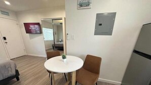 Une petite chambre moderne avec une table ronde, deux chaises, un lit, une télévision et un réfrigérateur.