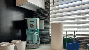 Une cuisine équipée d’une machine à café, de serviettes en papier et d’une fenêtre avec des stores.