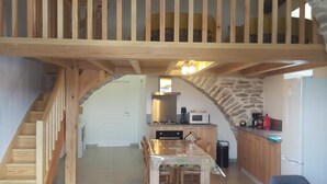 A spacious living area with a high wooden ceiling, a staircase leading to an upper level, a kitchen with stone accents, and a dining area. - Le P'tit Pelet, a house in the heart of the rocks (Fraissinet-de-Fourques)