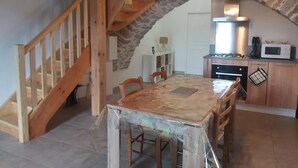 A rustic kitchen with a wooden staircase, a dining table, and a stone wall. - Le P'tit Pelet, a house in the heart of the rocks (Fraissinet-de-Fourques)