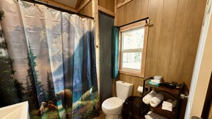 A bathroom with a forest-themed shower curtain, a white toilet, and a shelf with towels.
