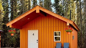 A small wooden cabin with a white door, numbered 4, and two blue chairs outside.