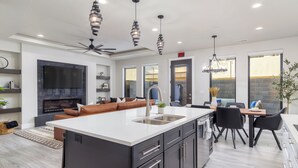Een moderne keuken met een groot eiland, inbouwapparatuur en een eetgedeelte met een kroonluchter.