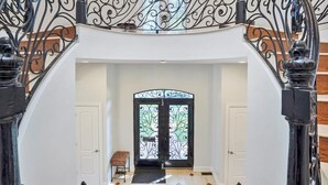 Ein beeindruckender Eingangsbereich mit einer schwarzen Metalltreppe, einem Schachbrettfußboden und einer verzierten Glas-Haustür.