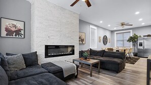 Una sala moderna con chimenea, sofás oscuros, una mesa de centro y una zona de comedor con refrigerador.