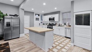 Cocina moderna con una isla central, electrodomésticos de acero inoxidable y suelo de baldosas.