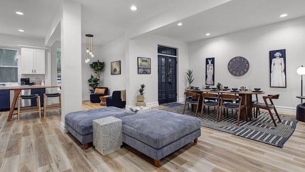 A modern living room with a dining area, featuring a large sofa set, a dining table with chairs, and a kitchen in the background. - 5BR St. Louis Home | Backyard Fire Pit + Games (St. Louis)