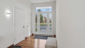 Un couloir avec un plancher en bois, un banc, une porte et une porte vitrée donnant sur l’extérieur.