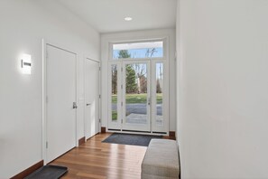 A hallway with a wooden floor, a bench, a door, and a glass door leading outside.