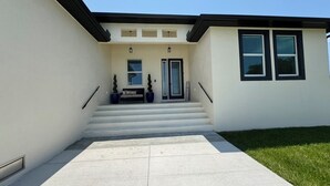 Una casa moderna de dos pisos con entrada de hormigón, una puerta principal y un pequeño porche.