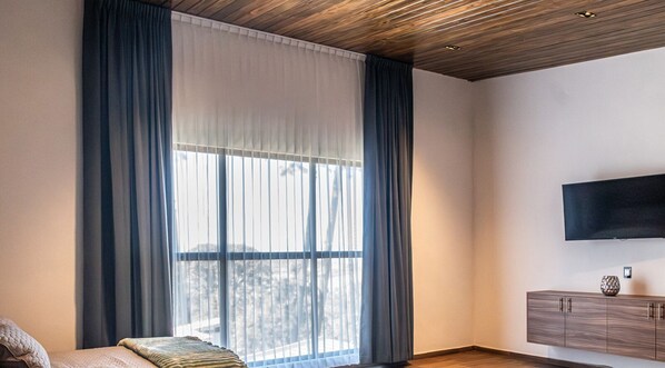 A modern room with a large window, a flat-screen TV mounted on the wall, and a wooden ceiling. - Spacious cottage in La Toscana Mazamitla (Mazamitla)