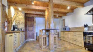 A rustic kitchen with exposed wooden beams, a brick wall, and a tiled floor. - Ain Amour de Bresse - DOMSURE (DOMSURE)