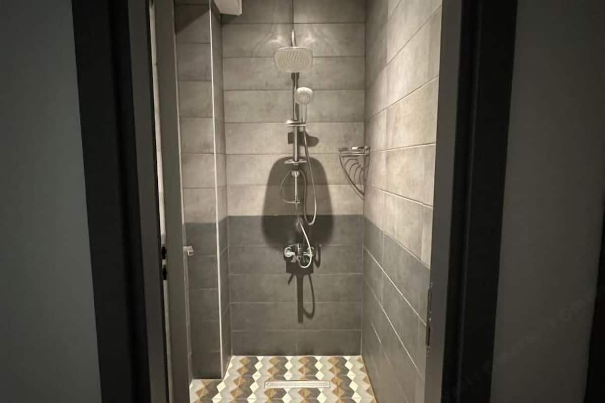 A small, tiled shower area with a handheld showerhead and a wall-mounted faucet.
