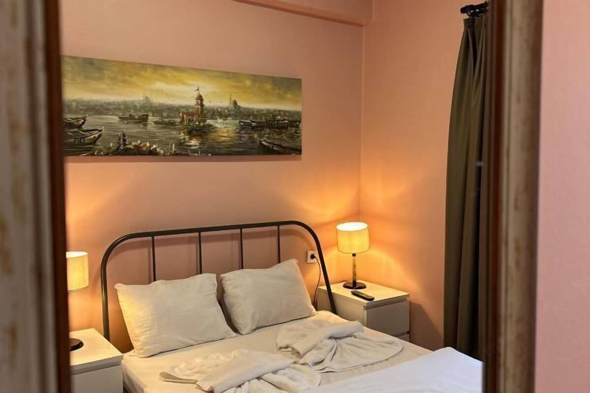 A hotel room with a bed, two bedside tables, a lamp, and a painting on the wall.