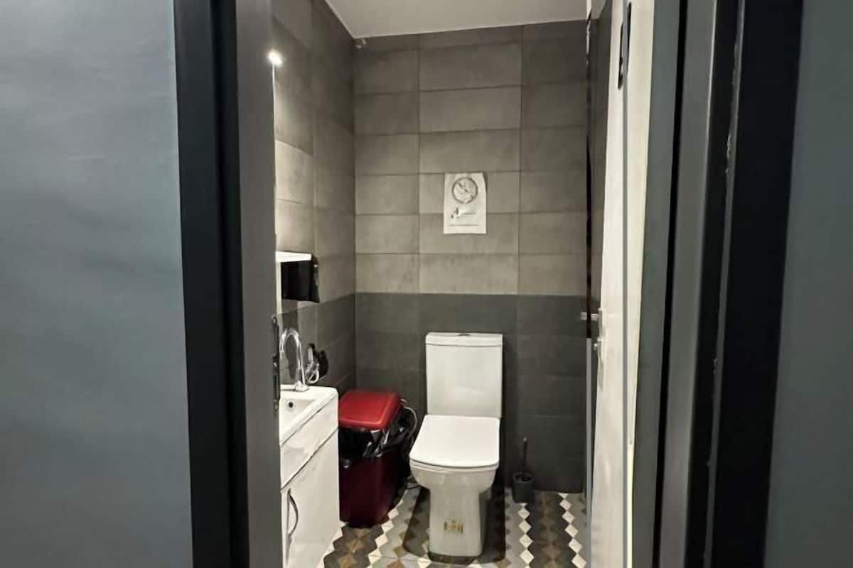 A bathroom with a toilet, a red suitcase, and a sink.