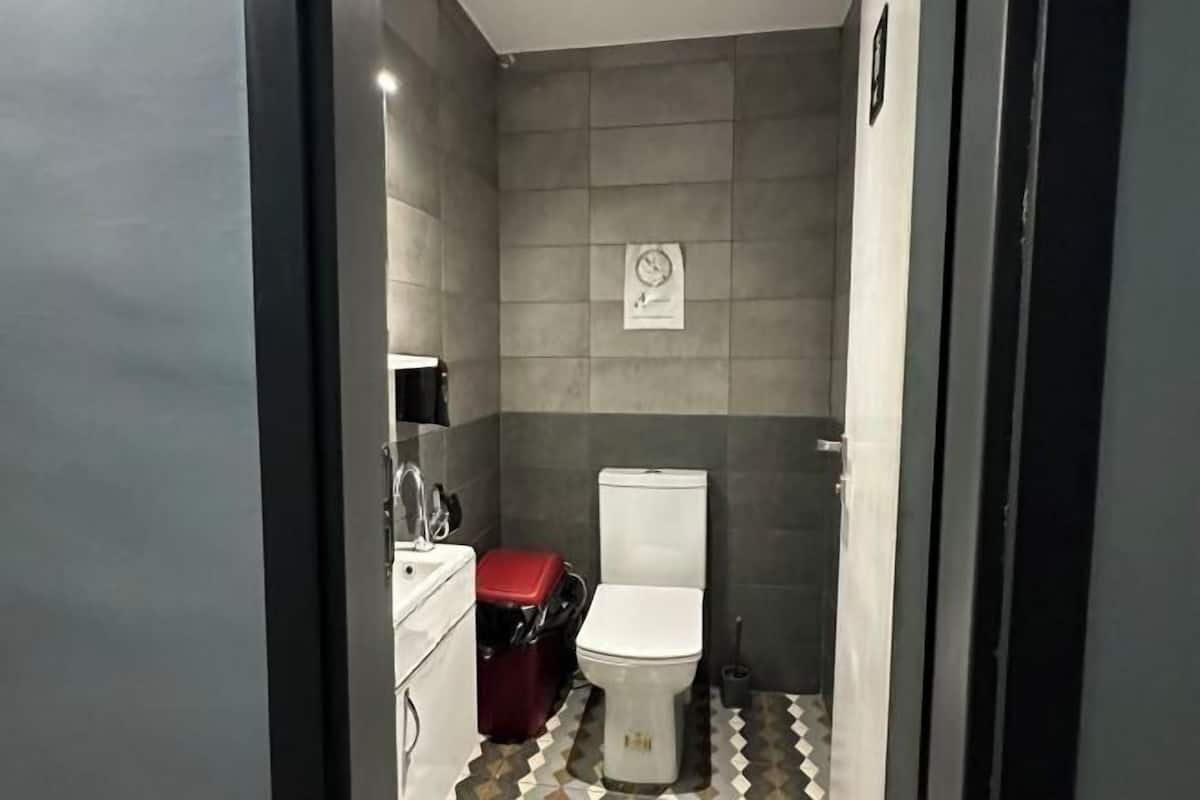 A compact bathroom with a toilet, a red suitcase, and a white sink.