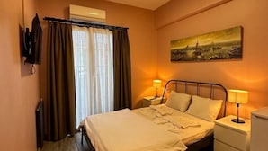 A hotel room with a bed, two bedside lamps, a painting on the wall, a window with curtains, and an air conditioning unit. - Archeo Cafe and Hostel (Istanbul)