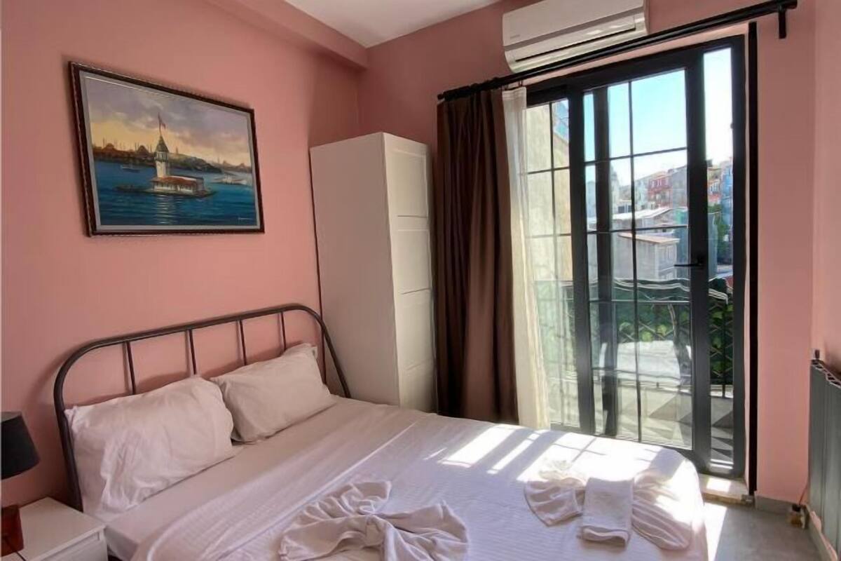 A bedroom with a bed, a painting, a wardrobe, and a view through a window.