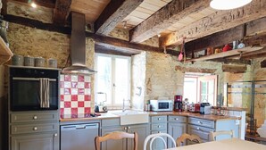 Una cocina rústica con paredes de piedra, vigas de madera, salpicadero de azulejos y electrodomésticos modernos.