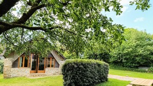 Una cabaña de piedra con una escalera de madera, un seto bien cuidado y una mesa de picnic en un jardín verde y frondoso.