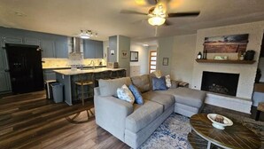 A modern kitchen with a dining area, a living room with a sectional sofa, and a fireplace.
