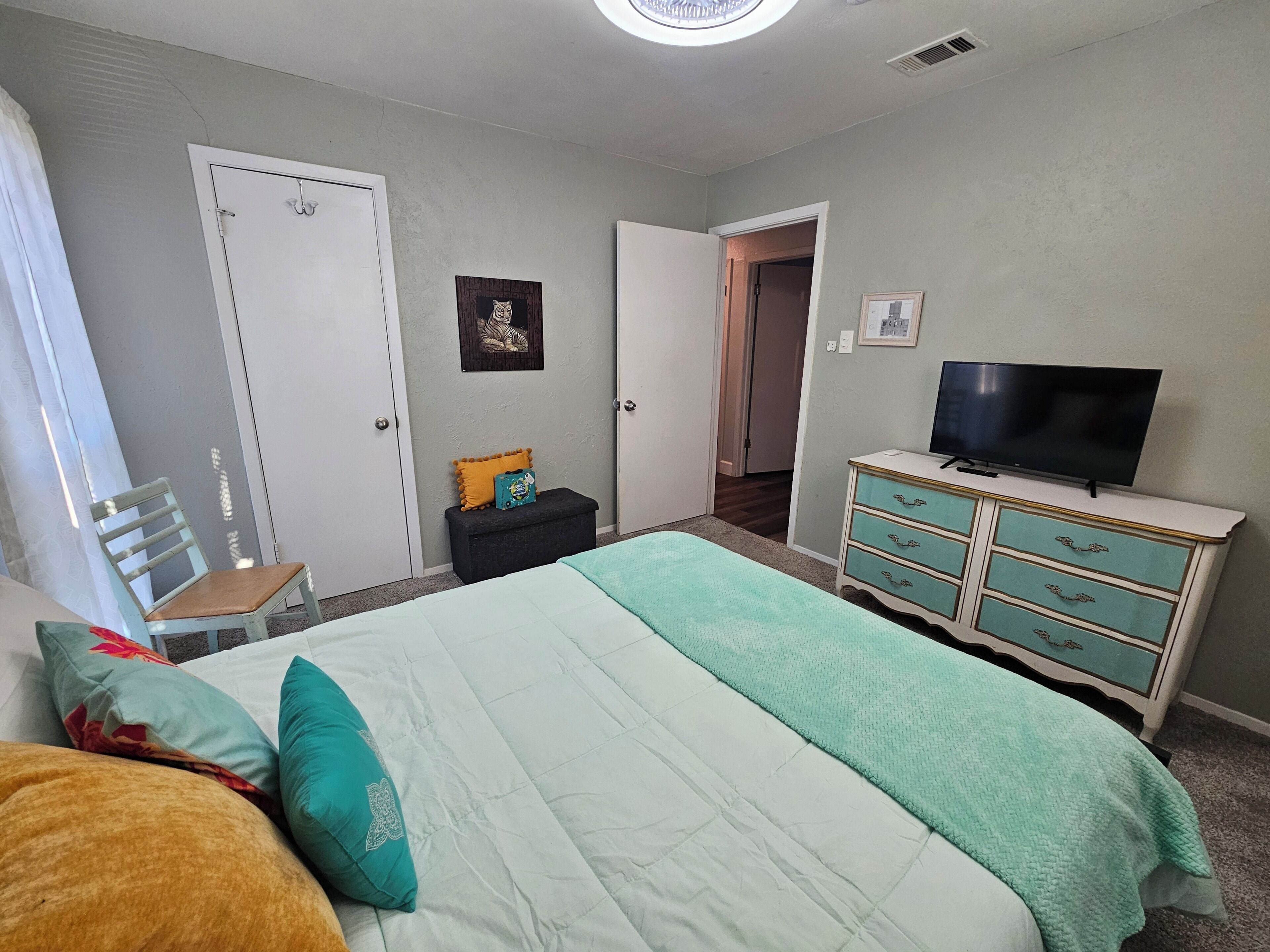 A bedroom with a bed, a dresser, a television, and a door leading to another room.
