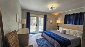 A bedroom with a bed, a desk, a chair, a lamp, and a view through a door.