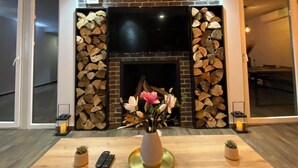 Ein modernes Wohnzimmer mit Kamin, einem runden Tisch mit Blumenvase und einem Fernseher, der über dem Kamin angebracht ist.