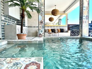 Ein Poolbereich mit gefliestem Boden, einer Palme und einer Sitzgelegenheit mit einer Couch und Tischen.