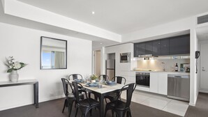 Une cuisine moderne avec des meubles blancs, des appareils en acier inoxydable et un coin repas avec une table dressée pour six personnes.