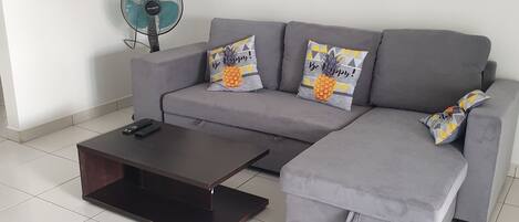 A modern living room with a grey sofa, two matching armchairs, a dark coffee table, and a small kitchen area in the background.