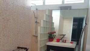 A bathroom with a shower, a sink with a mirror, and a red towel hanging on the wall.