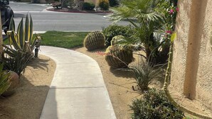 Une rue résidentielle bordée d’un trottoir, de palmiers et d’une maison dont le toit est recouvert de tuiles rouges.