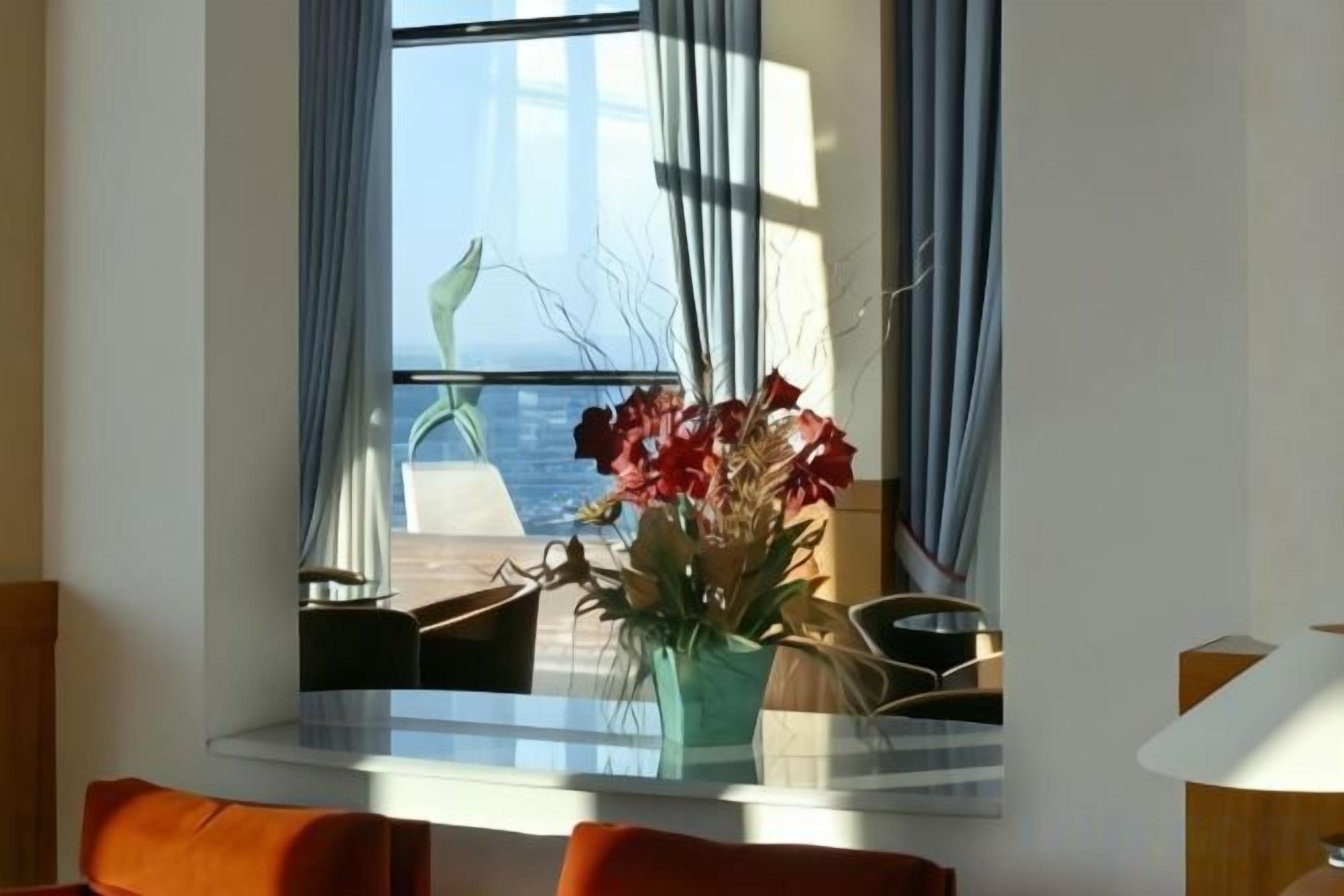 Un comedor con mesa, sillas, un jarrón con flores y vista al mar a través de una ventana.