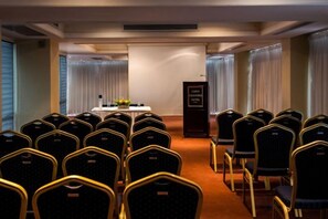 Un salón de conferencias con filas de sillas, un atril y una mesa con un micrófono.