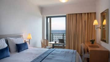Habitación de hotel con cama, dos lámparas de noche, un escritorio, una silla y vista al mar.