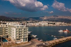 A coastal town with a modern building, marina, and mountains in the background.