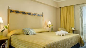 Habitación de hotel con cama, lámparas de noche, una silla, una mesita y un ventanal con cortinas.