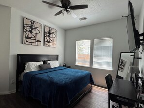 A bedroom with a bed, a desk, and a ceiling fan.