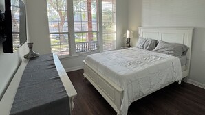 Un dormitorio con cama, escritorio, ventilador de techo y ventana con persianas.