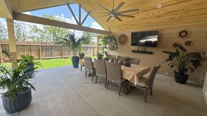 Un patio cubierto con una mesa y sillas para comer, rodeado de macetas con plantas.