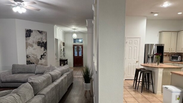 Una sala de estar moderna con un sofá seccional gris, una lámpara de pie blanca y un pasillo que conduce a una cocina con armarios blancos y un refrigerador de acero inoxidable.